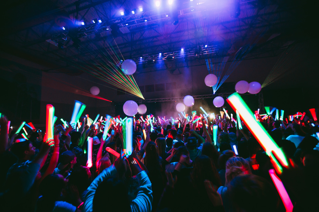 Audience holding colorful glow sticks beneath event lighting and lasers at a Living Energy event