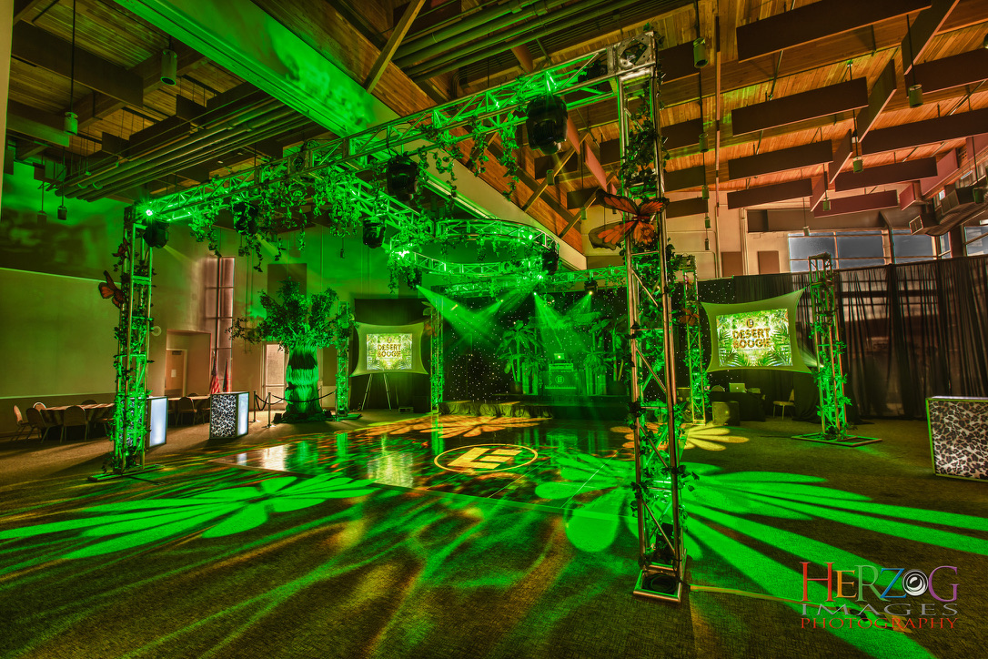 Living Energy event production setup with lighting trusses, green stage lights, and projection screens; Herzog Photography watermark visible